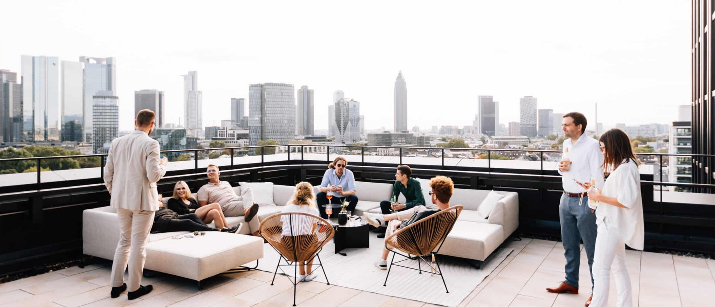 Personen im lockeren Small-Talk auf einer Dachterasse mit Sofalandschaft